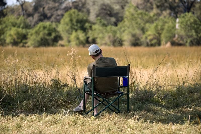 A trail participant sitting alone in a camp chair, looking out over the golden grass of the Okavango Delta